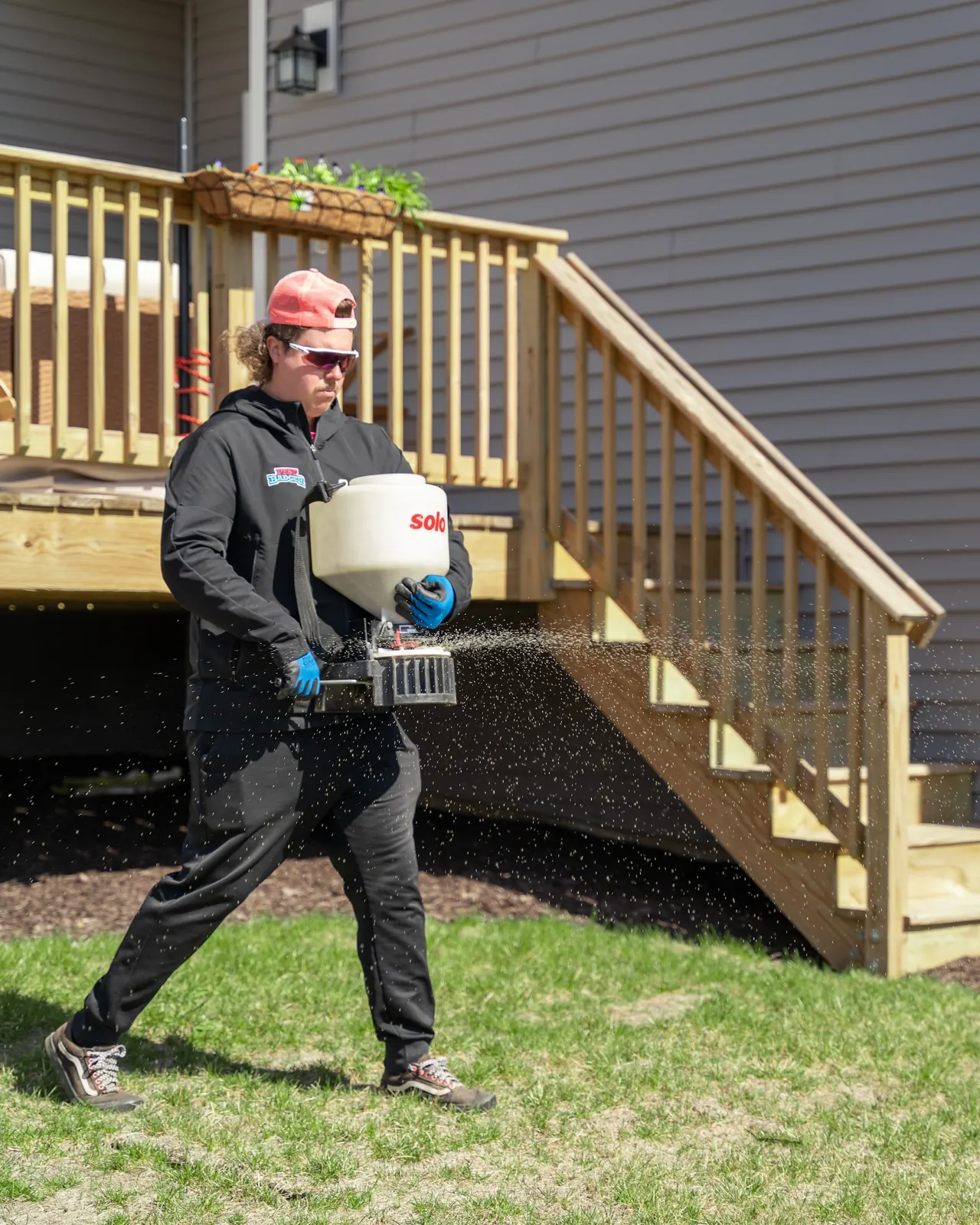 A technician spreading granules with a hand spreader past the back steps of a home