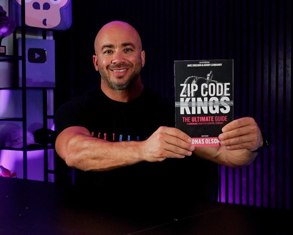 Smiling man in a black t-shirt holding up the book "Zip Code Kings: The Ultimate Guide to Growing Your Pest Control Company"